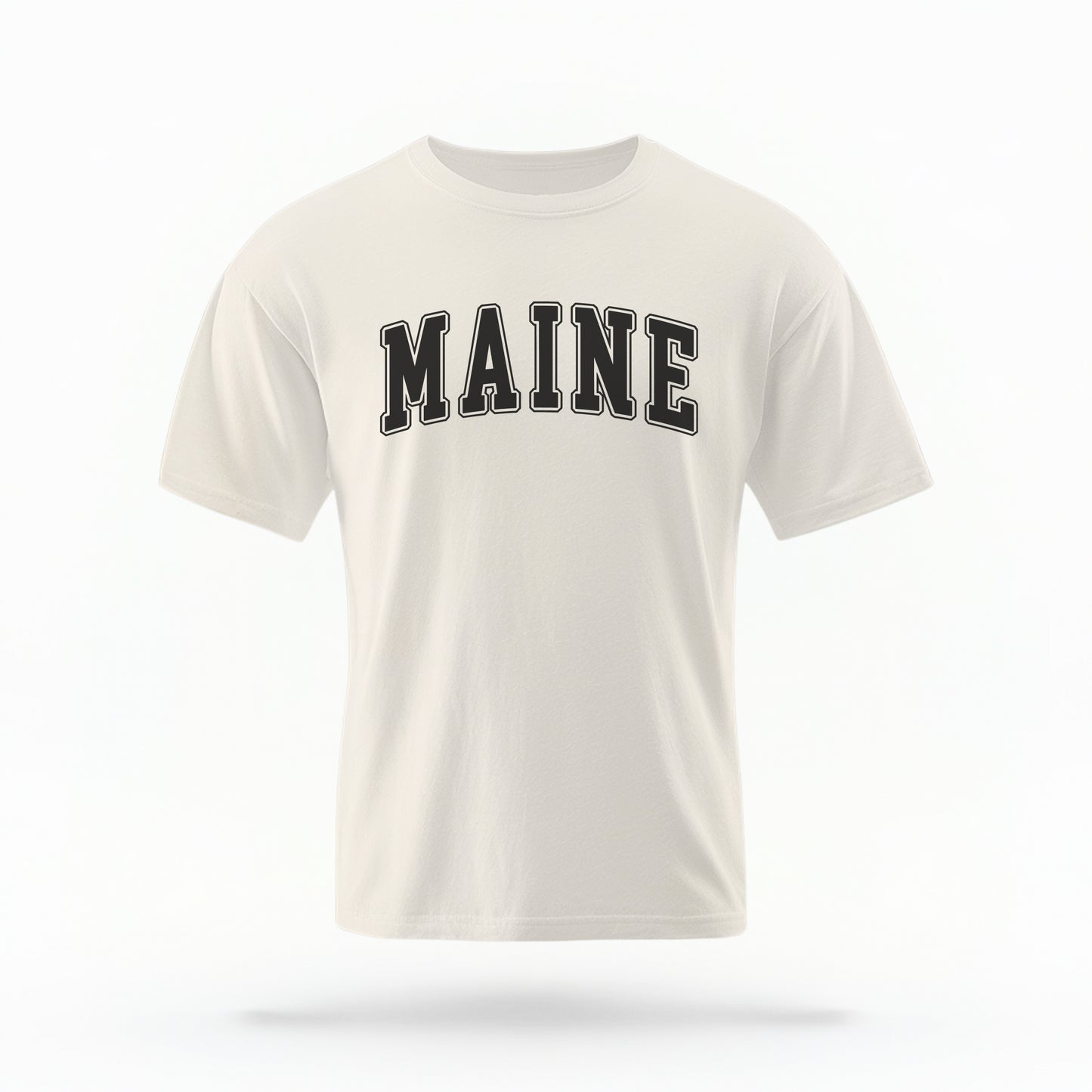 The ivory Unisex Maine Varsity Comfort Colors T-shirt lays flat on a white background. The Maine graphic is in bold black in a varsity offset style.