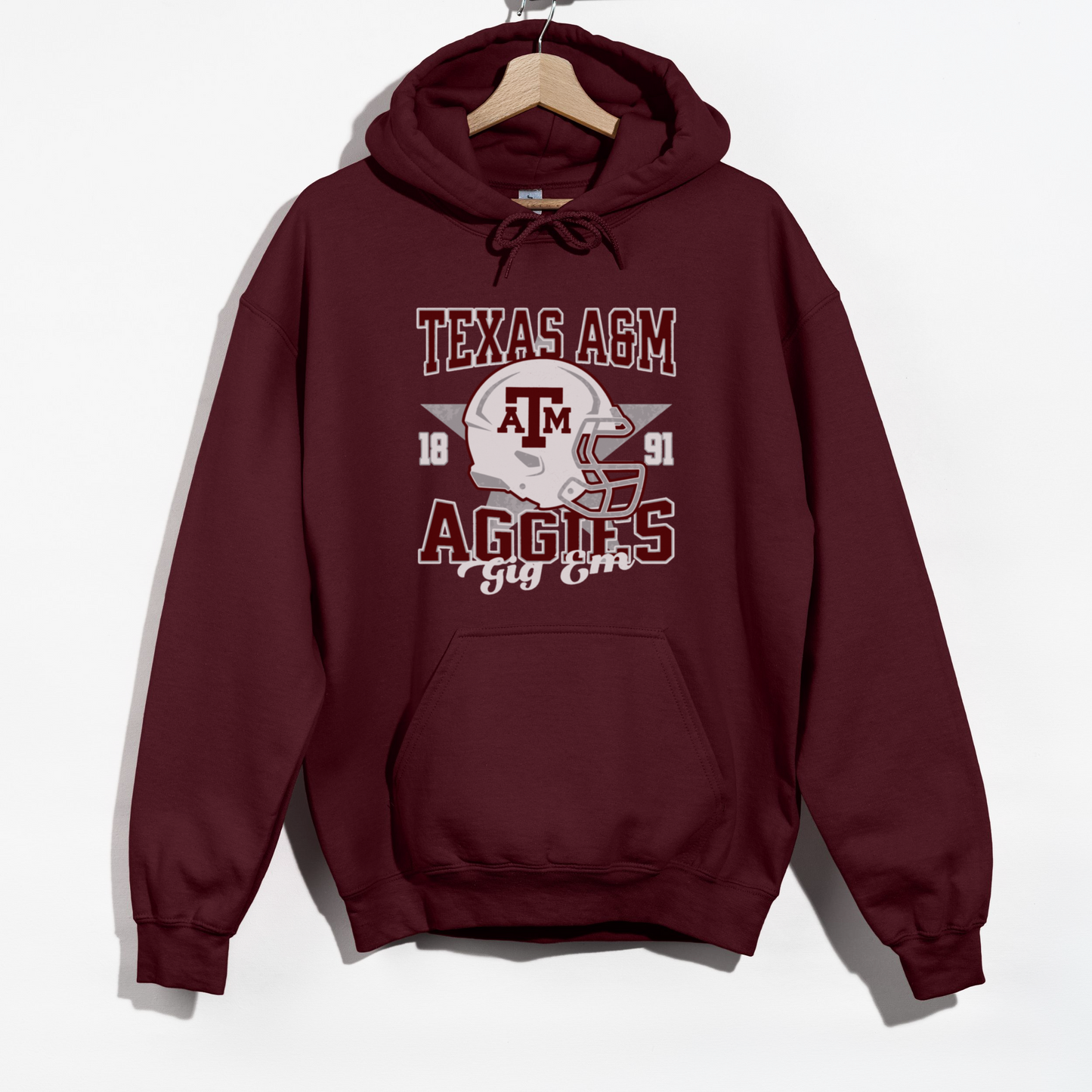 The Maroon Texas A&M Aggies Football Hoodie Sweatshirt lays flat on a white background. The Texas A&M Aggies Football graphic is in bold Unisex in a Varsity style.