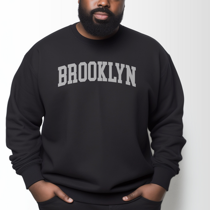 A model wears the Black Adult Unisex Brooklyn NY Collegiate Crewneck Sweatshirt.  The ﻿Brooklyn NY Collegiate﻿ graphic is in bold White in a Varsity style.