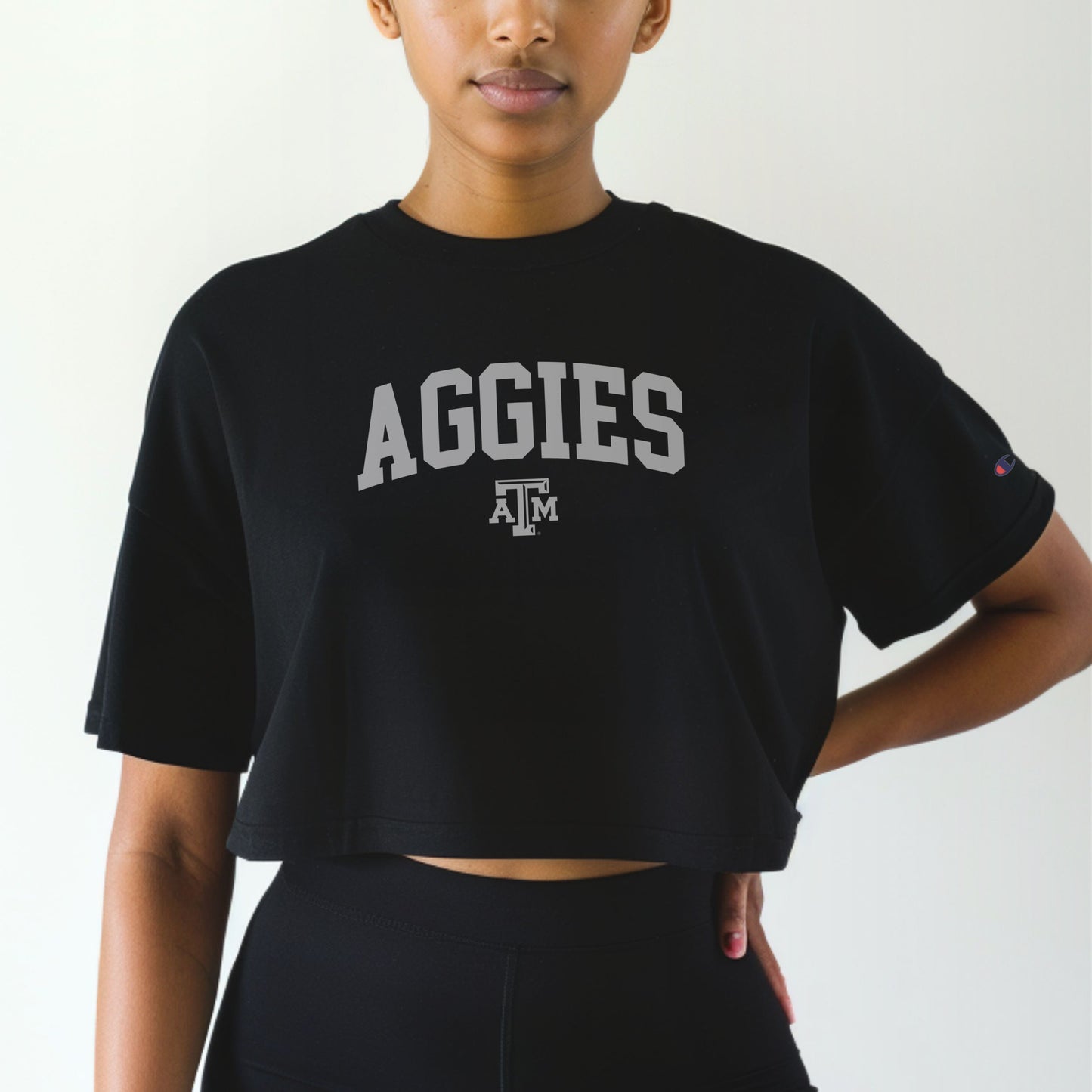 A model wears the Black Adult Womens Texas A&M Aggies Collegiate Crop Top.  The ﻿Texas A&M Aggies Collegiate﻿ graphic is in bold White in a Varsity style.