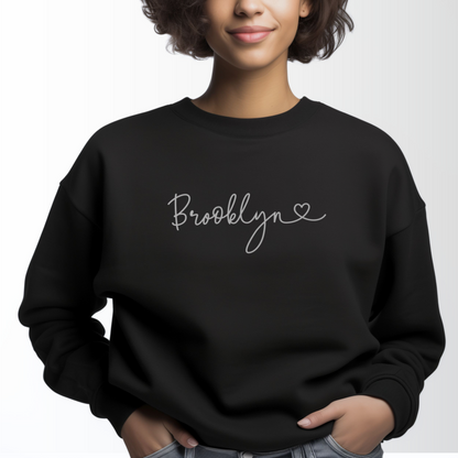 A model wears the Black Adult Unisex Brooklyn NY Dainty Crewneck Sweatshirt.  The ﻿Brooklyn NY Dainty﻿ graphic is in bold White in a Script style.