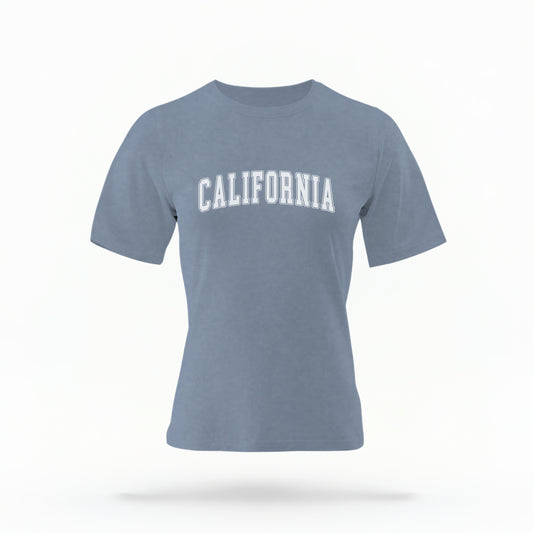 The Blue Jean California Varsity Comfort Colors T-shirt lays flat on a white background. The ﻿California Varsity﻿ graphic is in bold White in a Varsity style.