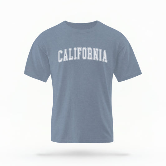 The Blue Jean California Varsity Comfort Colors T-shirt lays flat on a white background. The ﻿California Varsity﻿ graphic is in bold White in a Varsity style.