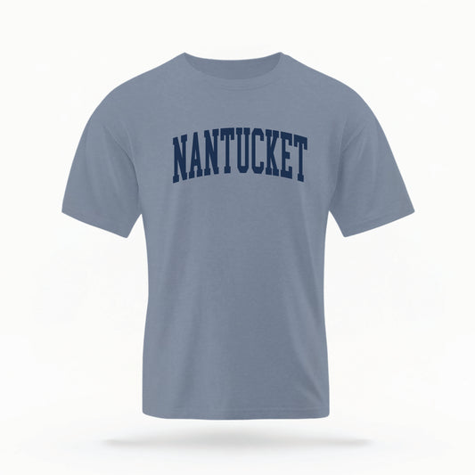 The Blue Jean Adult Unisex Nantucket Massachusetts Varsity Comfort Colors T-shirt lays flat on a white background. The ﻿Nantucket Massachusetts Varsity﻿ graphic is in bold Navy in a Collegiate Block style.