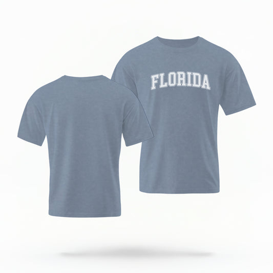The blue-jeans Adult Unisex Florida Varsity Comfort Colors T-shirt lays flat on a white background. The Florida graphic is in bold white in a varsity offset style.