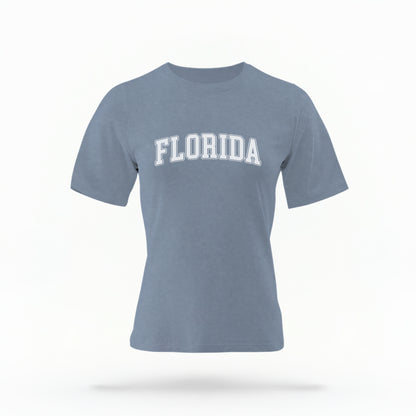 The blue jeans Adult Unisex Florida Varsity Comfort Colors T-shirt lays flat on a white background. The Florida graphic is in bold white in a varsity offset style.