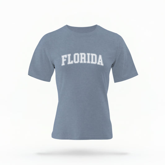 The blue jeans Adult Unisex Florida Varsity Comfort Colors T-shirt lays flat on a white background. The Florida graphic is in bold white in a varsity offset style.