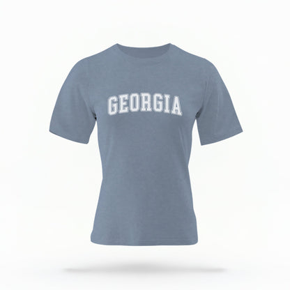 The Blue Jeans Unisex Georgia Varsity Comfort Colors T-shirt lays flat on a white background. The Georgia graphic is in bold white in a varsity offset style.
