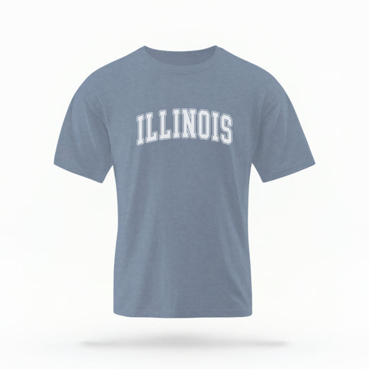 The Blue Jeans Unisex Illinois Varsity Comfort Colors T-shirt lays flat on a white background. The Illinois graphic is in bold white in a varsity offset style.