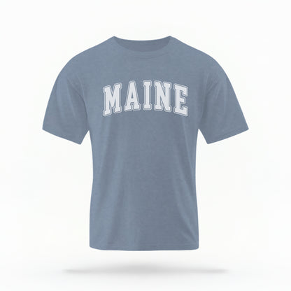 The Blue Jeans Unisex Maine Varsity Comfort Colors T-shirt lays flat on a white background. The Maine graphic is in bold white in a varsity offset style.