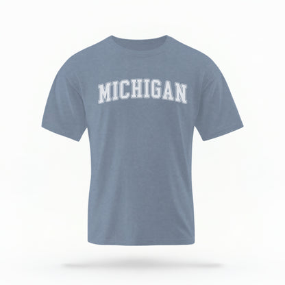 The Blue Jeans Unisex Michigan Varsity Comfort Colors T-shirt lays flat on a white background. The Michigan graphic is in bold white in a varsity offset style.