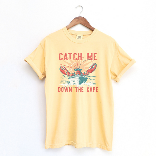 The Butter Adult Unisex Catch Me Down The Cape Comfort Colors T-shirt lays flat on a white background. The ﻿Catch Me Down The Cape﻿ graphic is in bold Lifestyle in a Vintage style.