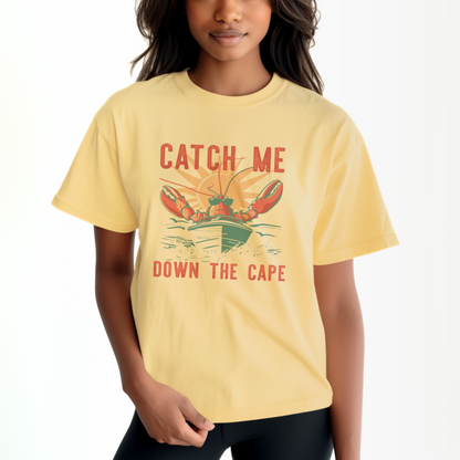 The Butter Adult Unisex Catch Me Down The Cape Comfort Colors T-shirt lays flat on a white background. The ﻿Catch Me Down The Cape﻿ graphic is in bold multicolor in a Vintage style.