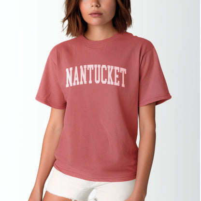 A model wears the Crimson Adult Unisex Nantucket Massachusetts Varsity Comfort Colors T-shirt.  The ﻿Nantucket Massachusetts Varsity﻿ graphic is in bold White in a Collegiate Block style.