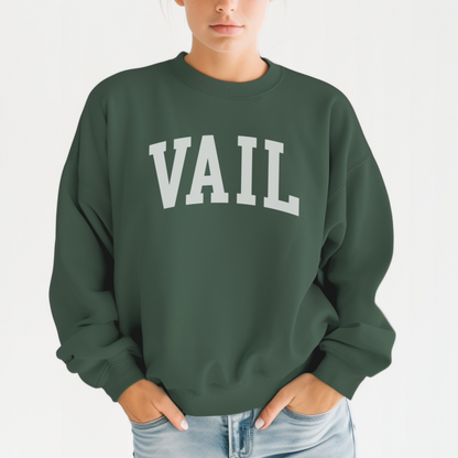 A model wears the Forest Green Vail Colorado Varsity Crewneck Sweatshirt.  The ﻿Vail Colorado Varsity﻿ graphic is in bold White in a Collegiate style.