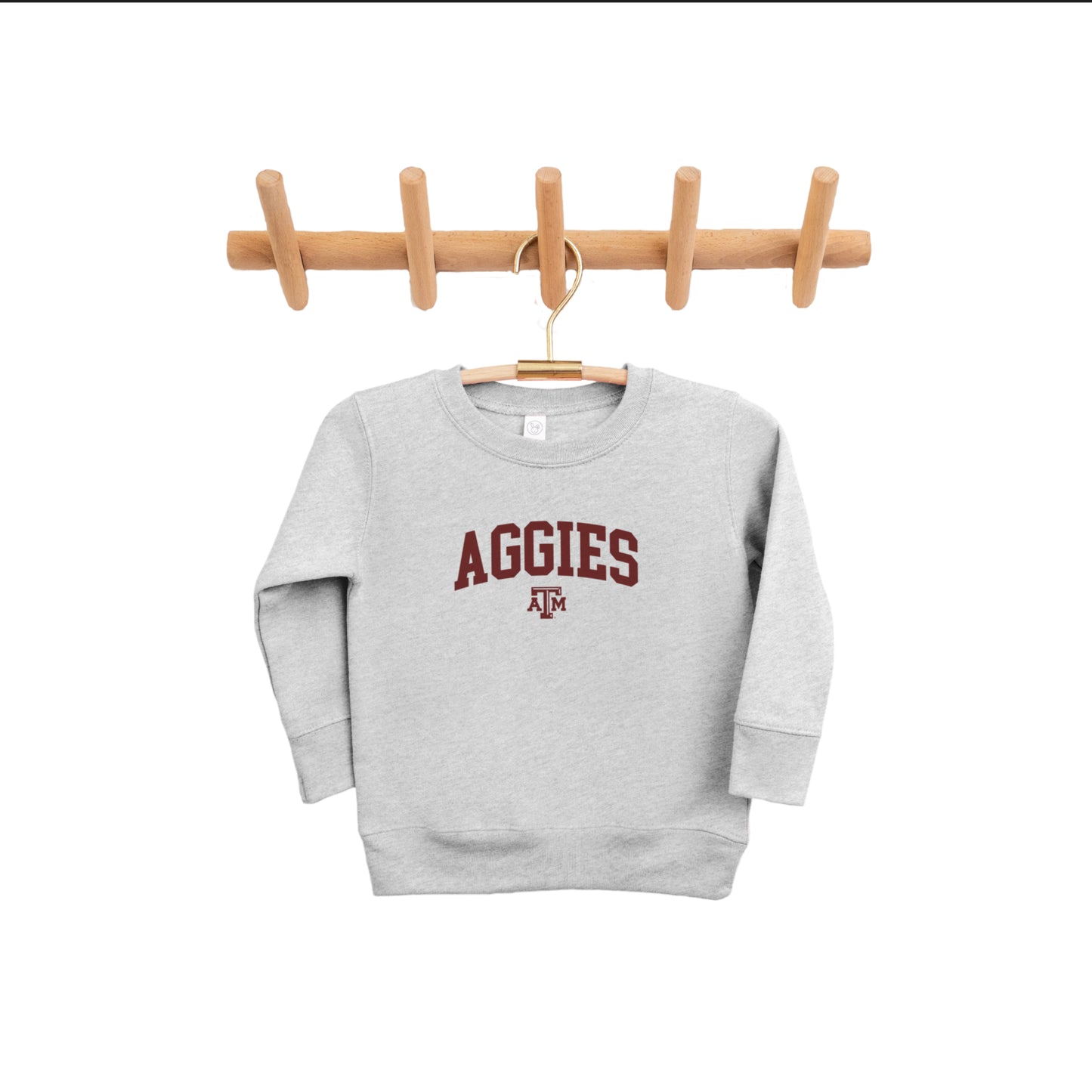 The gray Toddler Texas A&M Aggies Collegiate Crewneck Sweatshirt hangs from a pine clothing rack.  The ﻿Texas A&M Aggies Collegiate﻿ graphic is in bold Maroon in a Varsity style.