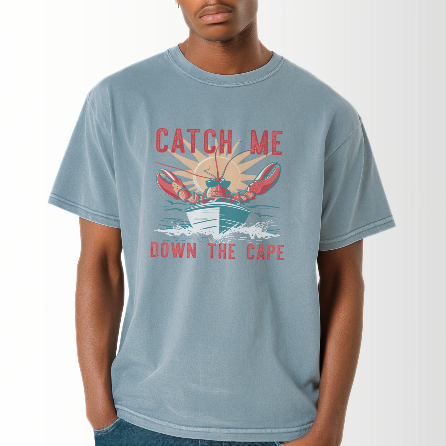 A model wears the Ice Blue Adult Unisex Catch Me Down The Cape Comfort Colors T-shirt.  The ﻿Catch Me Down The Cape﻿ graphic is in bold multicolors in a Vintage style.