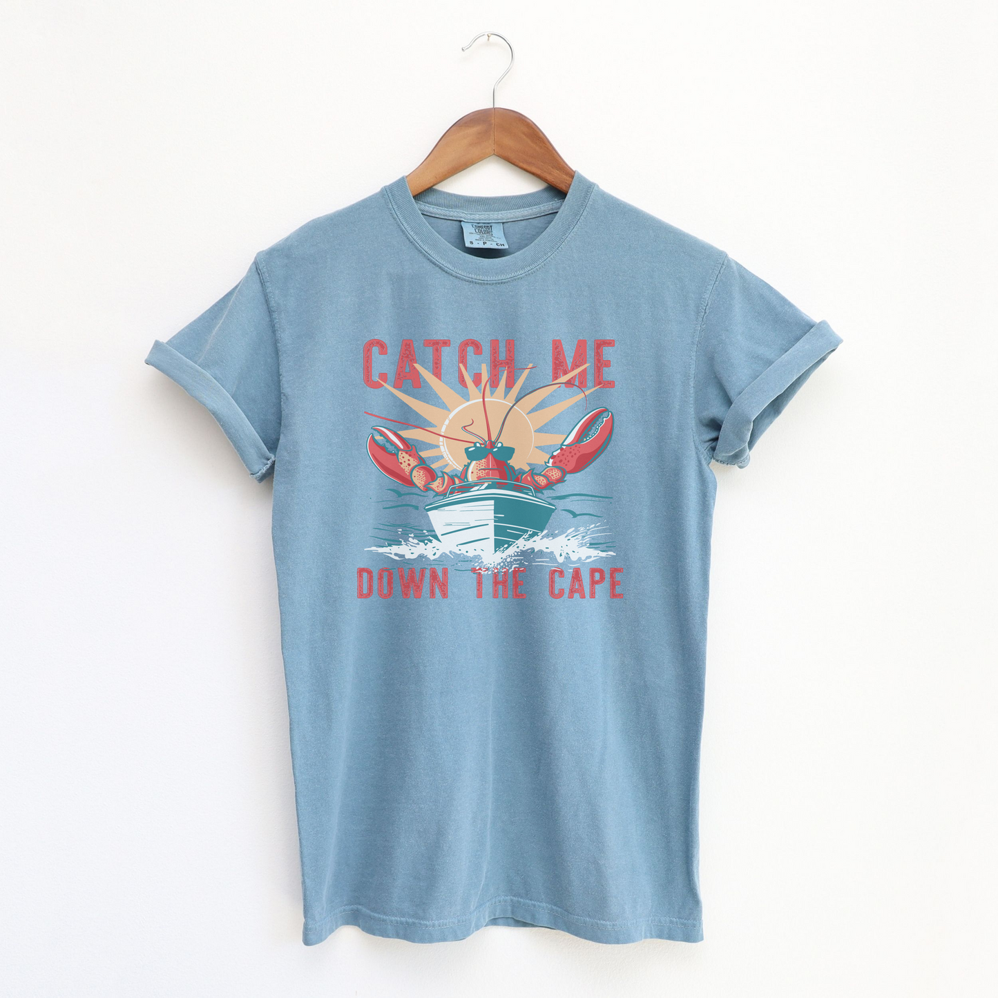 The Ice Blue Adult Unisex Catch Me Down The Cape Comfort Colors T-shirt lays flat on a white background. The ﻿Catch Me Down The Cape﻿ graphic is in bold Lifestyle in a Vintage style.