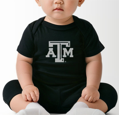 A model wears the Black Infant Unisex Texas A&M Logo Bodysuit.  The ﻿Texas A&M Logo﻿ graphic is in bold White in a Varsity style.