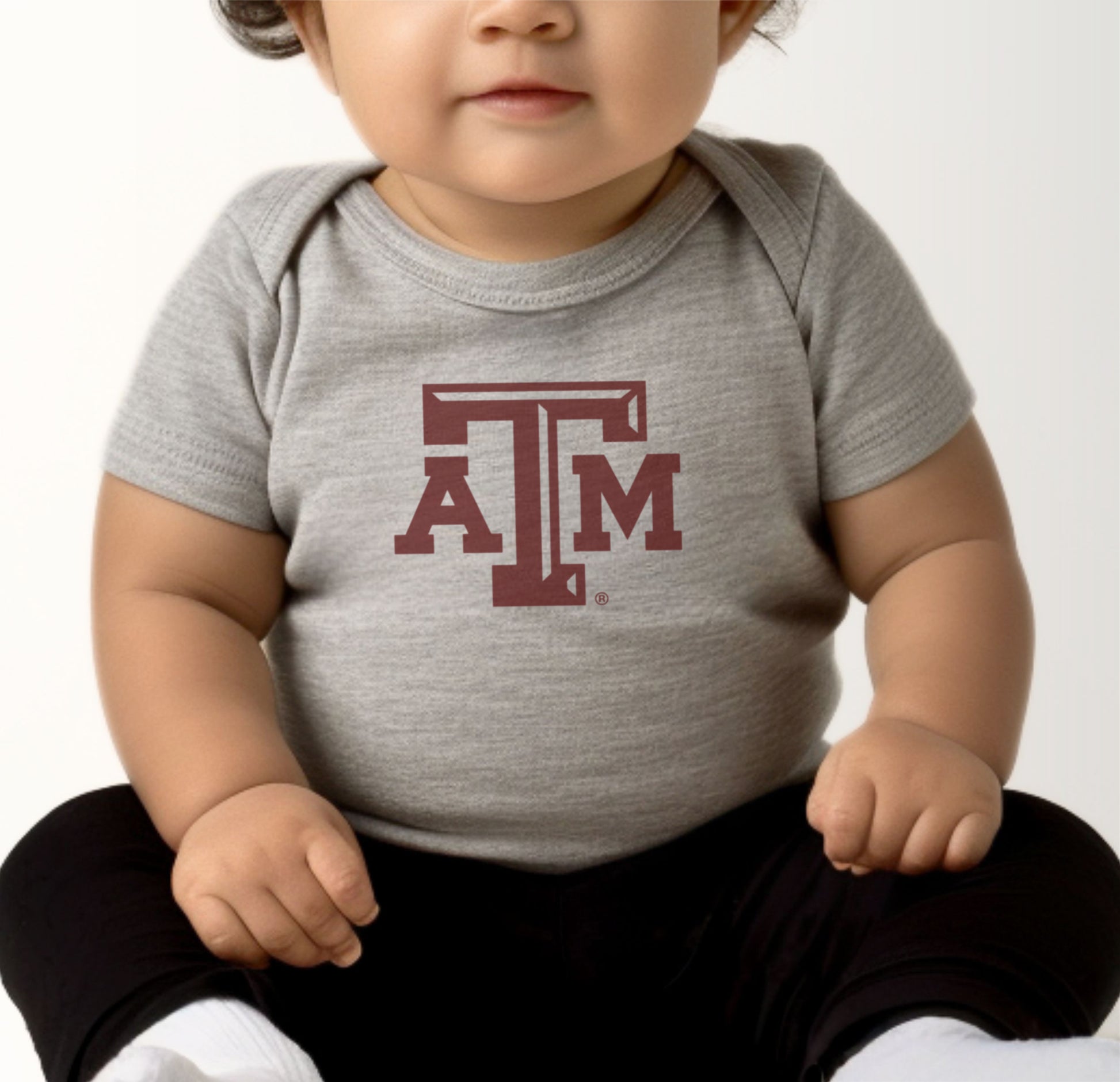 A model wears the Heather Grey Infant Unisex Texas A&M Logo Bodysuit.  The ﻿Texas A&M Logo﻿ graphic is in bold Maroon in a Varsity style.