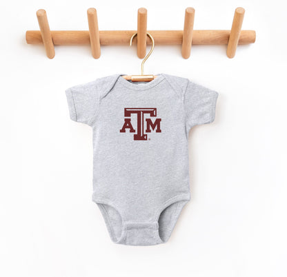 The Heather Grey Infant Unisex Texas A&M Logo Bodysuit lays flat on a white background. The ﻿Texas A&M Logo﻿ graphic is in bold Maroon in a Varsity style.