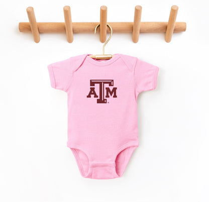 The Pink Infant Unisex Texas A&M Logo Bodysuit lays flat on a white background. The ﻿Texas A&M Logo﻿ graphic is in bold Maroon in a Varsity style.