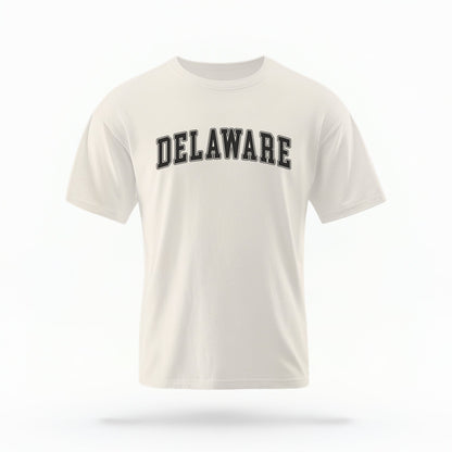 The ivory Unisex Delaware Varsity Comfort Colors T-shirt lays flat on a white background. The Delaware graphic is in bold black in a varsity offset style.