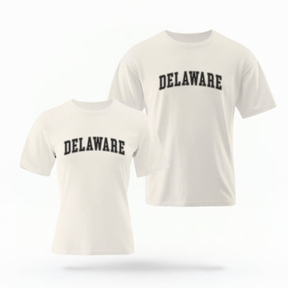 The ivory Unisex Delaware Varsity Comfort Colors T-shirt lays flat on a white background. The Delaware graphic is in bold black in a varsity offset style.