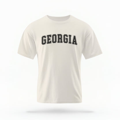 The ivory Unisex Georgia Varsity Comfort Colors T-shirt lays flat on a white background. The Georgia graphic is in bold black in a varsity offset style.