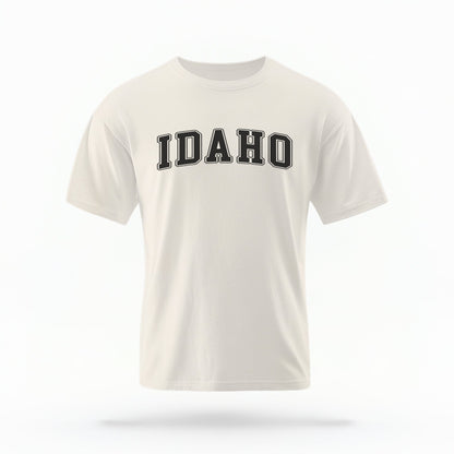 The ivory Unisex Idaho Varsity Comfort Colors T-shirt lays flat on a white background. The Idaho graphic is in bold black in a varsity offset style.