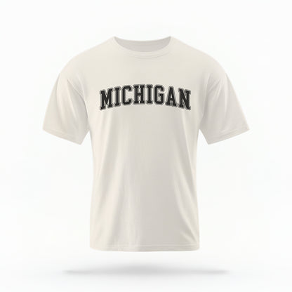 The ivory Unisex Michigan Varsity Comfort Colors T-shirt lays flat on a white background. The Michigan graphic is in bold black in a varsity offset style.