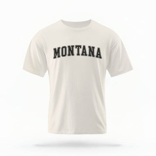 The ivory Unisex Montana Varsity Comfort Colors T-shirt lays flat on a white background. The Montana graphic is in bold black in a varsity offset style.