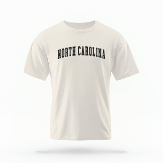 The ivory Unisex North Carolina Varsity Comfort Colors T-shirt lays flat on a white background. The North Carolina graphic is in bold black in a varsity offset style.

