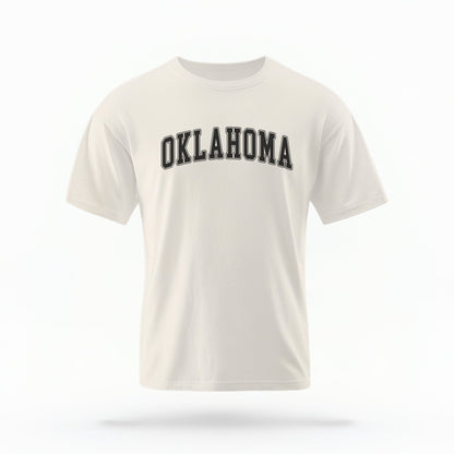 The ivory Unisex Oklahoma Varsity Comfort Colors T-shirt lays flat on a white background. The Oklahoma graphic is in bold black in a varsity offset style.