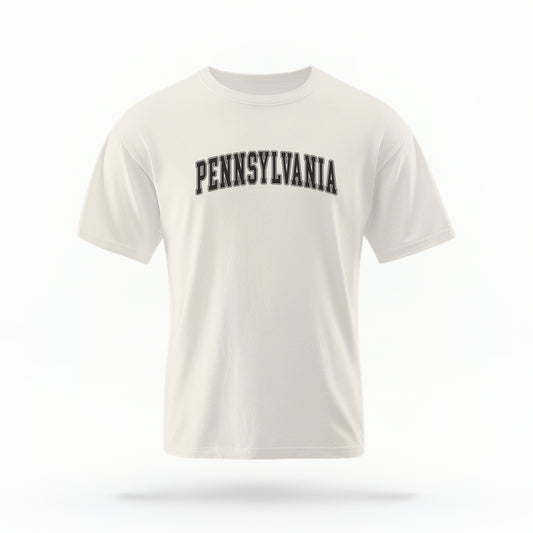 The ivory Unisex Pennsylvania Varsity Comfort Colors T-shirt lays flat on a white background. The Pennsylvania graphic is in bold black in a varsity offset style.