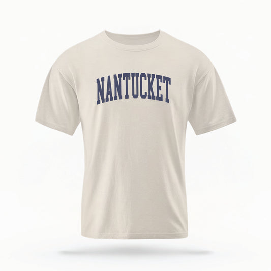 The Ivory Adult Unisex Nantucket Massachusetts Varsity Comfort Colors T-shirt lays flat on a white background. The ﻿Nantucket Massachusetts Varsity﻿ graphic is in bold Navy in a Collegiate Block style.