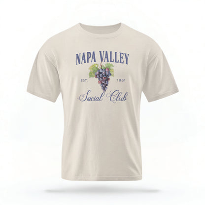 The Ivory Adult Unisex Napa Valley Wineries Social Club T-shirt stands against a white background.  The Napa Valley grapes  graphic is in bold purple and green in a  preppy old money style. 