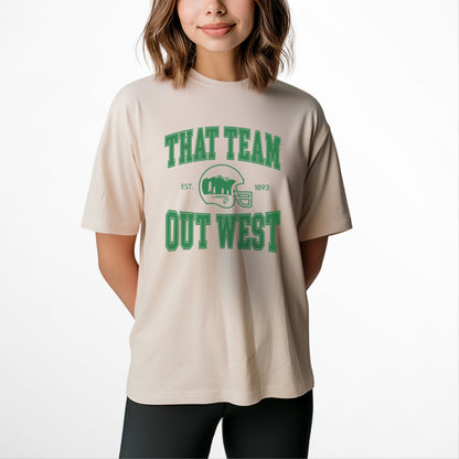 A womens model wears the That team out west Comfort Colors T-shirt. The graphic is in green  in a collegiate style.