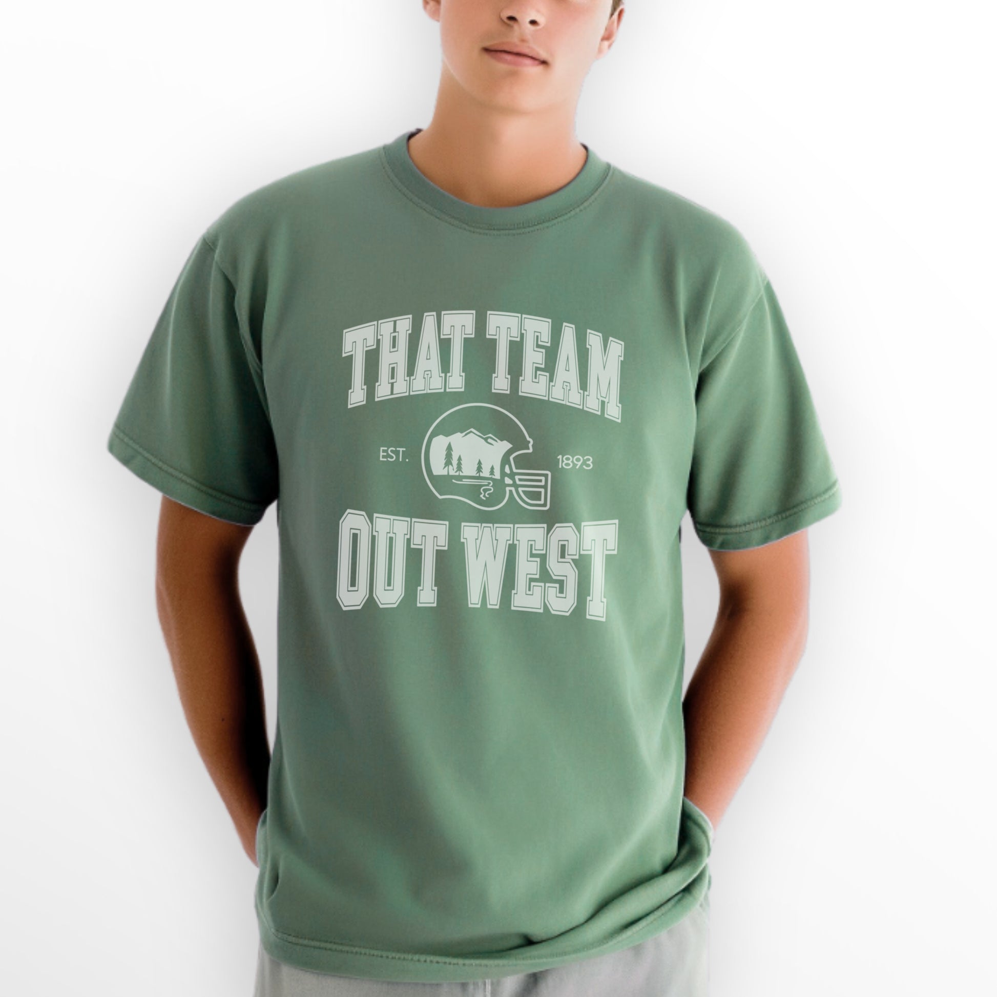 A mens model wears the That team out west Comfort Colors T-shirt. The graphic is in White  in a collegiate style.