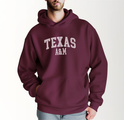 A model wears the Maroon Adult Unisex Texas A&M Varsity Hooded Sweatshirt.  The ﻿Texas A&M Varsity﻿ graphic is in bold White in a Collegiate style.