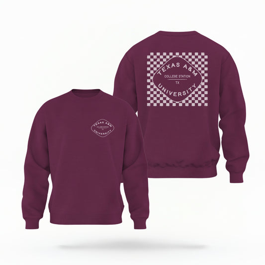 A maroon Texas A&M Crewneck Sweatshirt lays flat on white background. The graphic contains a retro checkered pattern. 