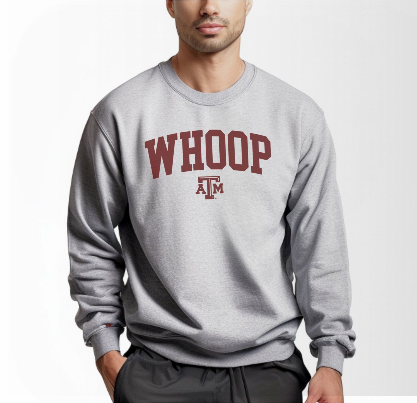 A model wears the Sport Grey Adult Unisex Texas A&M Whoop Collegiate Crewneck Sweatshirt.  The ﻿Texas A&M Whoop Collegiate﻿ graphic is in bold Maroon in a Varsity style.