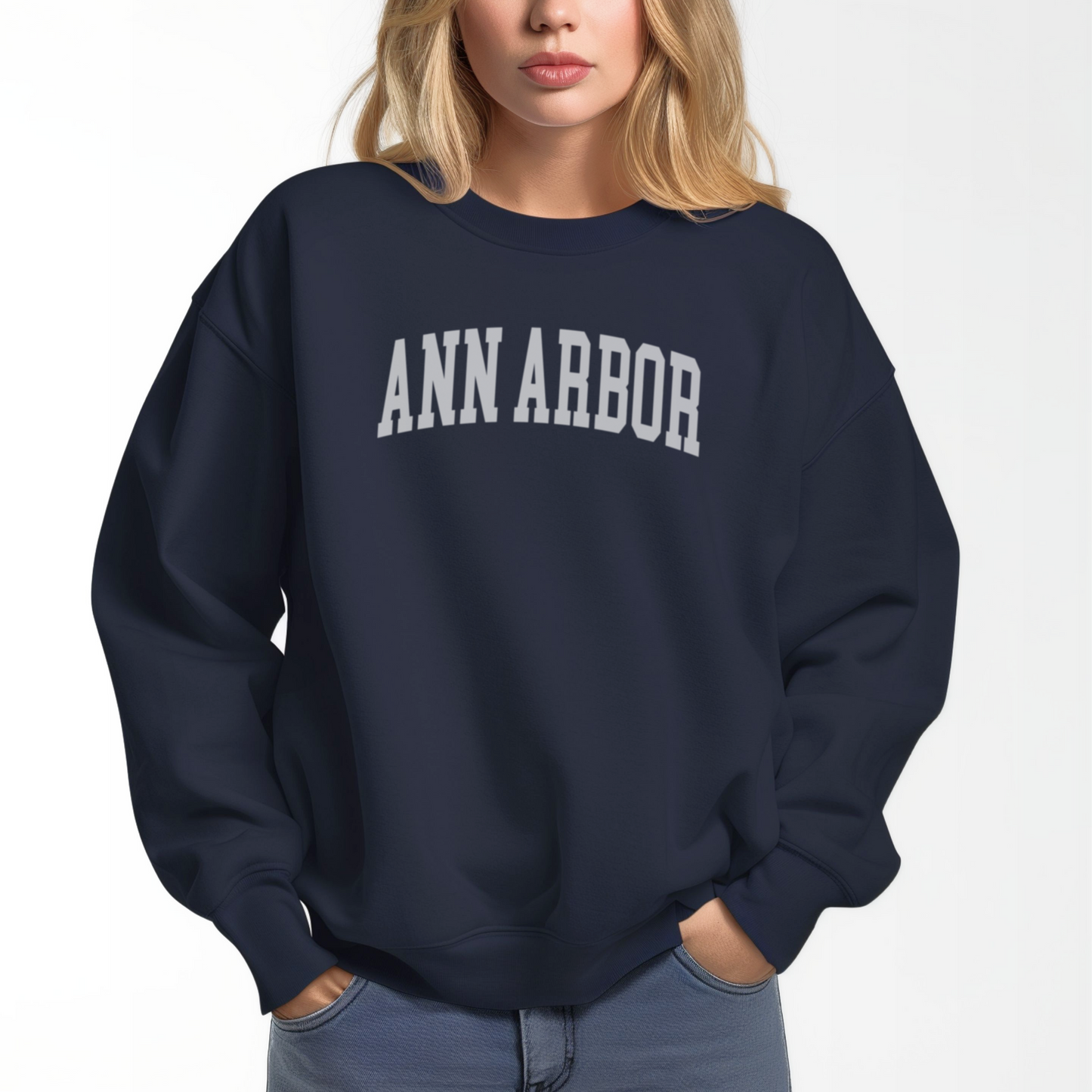 A model wears the Navy Adult Unisex Ann Arbor Michigan Varsity Crewneck Sweatshirt. The Ann Arbor Michigan Varsity graphic is in bold White in a Collegiate style.