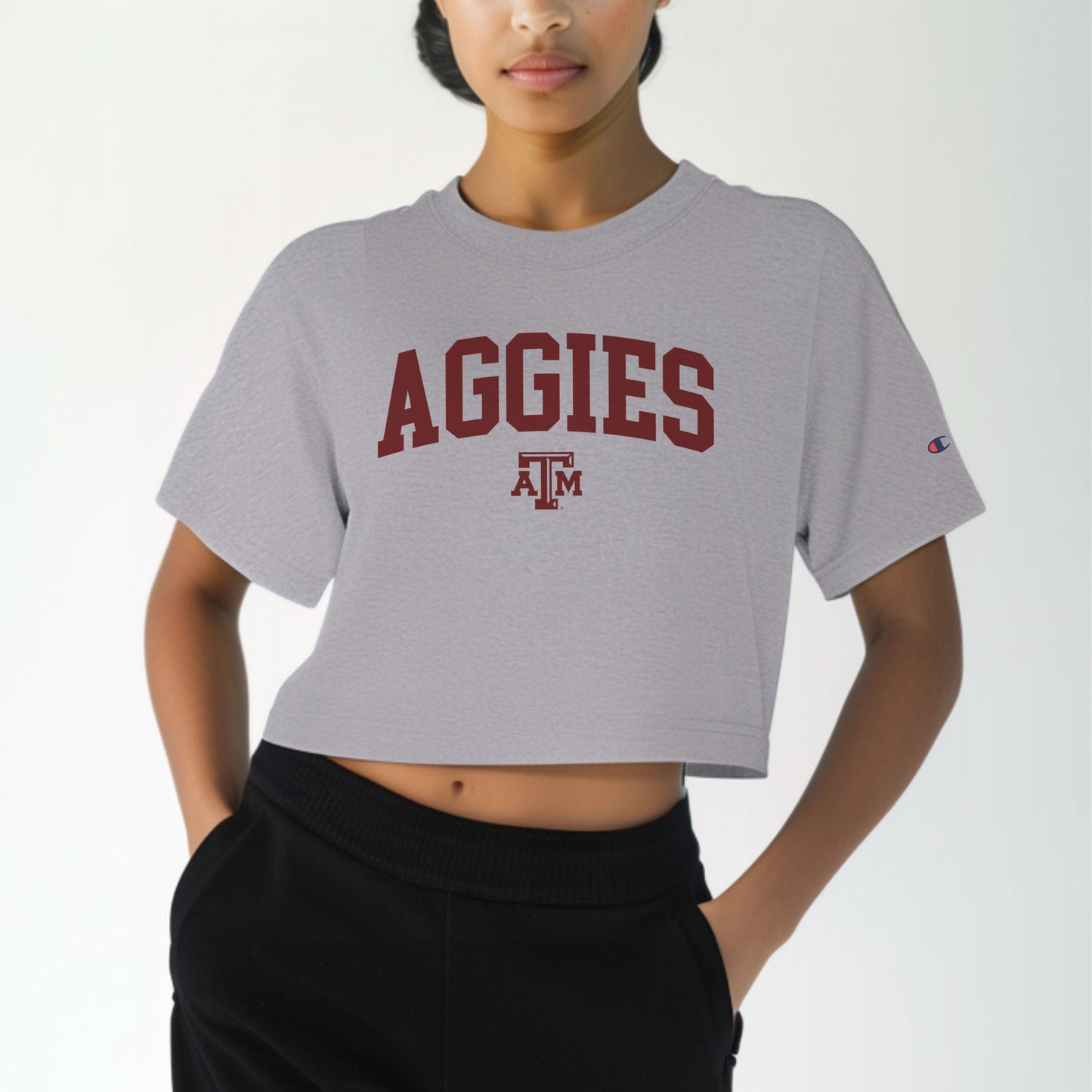 A model wears the Oxford Grey Adult Womens Texas A&M Aggies Collegiate Crop Top. The ﻿Texas A&M Aggies Collegiate﻿ graphic is in bold Maroon in a Varsity style.