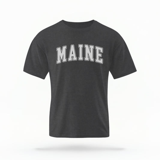 The Pepper Unisex Maine Varsity Comfort Colors T-shirt lays flat on a white background. The Maine graphic is in bold white in a varsity offset style.
