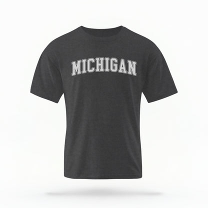 The Pepper Unisex Michigan Varsity Comfort Colors T-shirt lays flat on a white background. The Michigan graphic is in bold white in a varsity offset style.