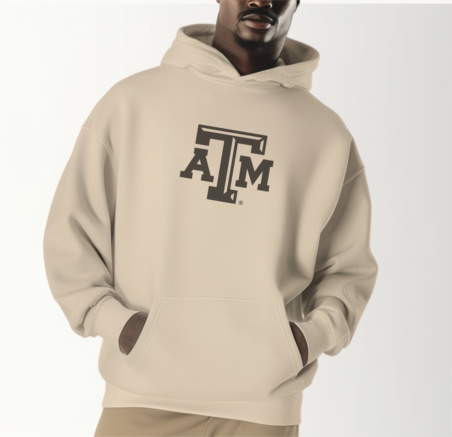 A model wears the Sand Adult Unisex Texas A&M Logo Hooded Sweatshirt.  The ﻿Texas A&M Logo﻿ graphic is in bold Black in a Varsity style.