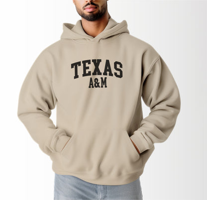 A model wears the Sand Adult Unisex Texas A&M Varsity Hooded Sweatshirt.  The ﻿Texas A&M Varsity﻿ graphic is in bold Black in a Collegiate style.