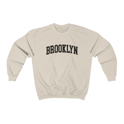 The Sand Adult Unisex Brooklyn NY Collegiate Crewneck Sweatshirt lays flat on a white background. The ﻿Brooklyn NY Collegiate﻿ graphic is in bold Black in a Varsity style.