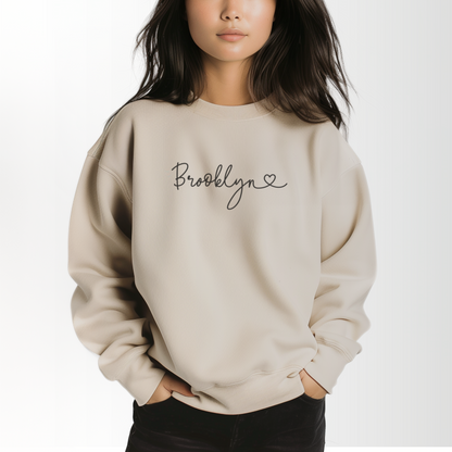 A model wears the Sand Adult Unisex Brooklyn NY Dainty Crewneck Sweatshirt.  The ﻿Brooklyn NY Dainty﻿ graphic is in bold Black in a Script style.